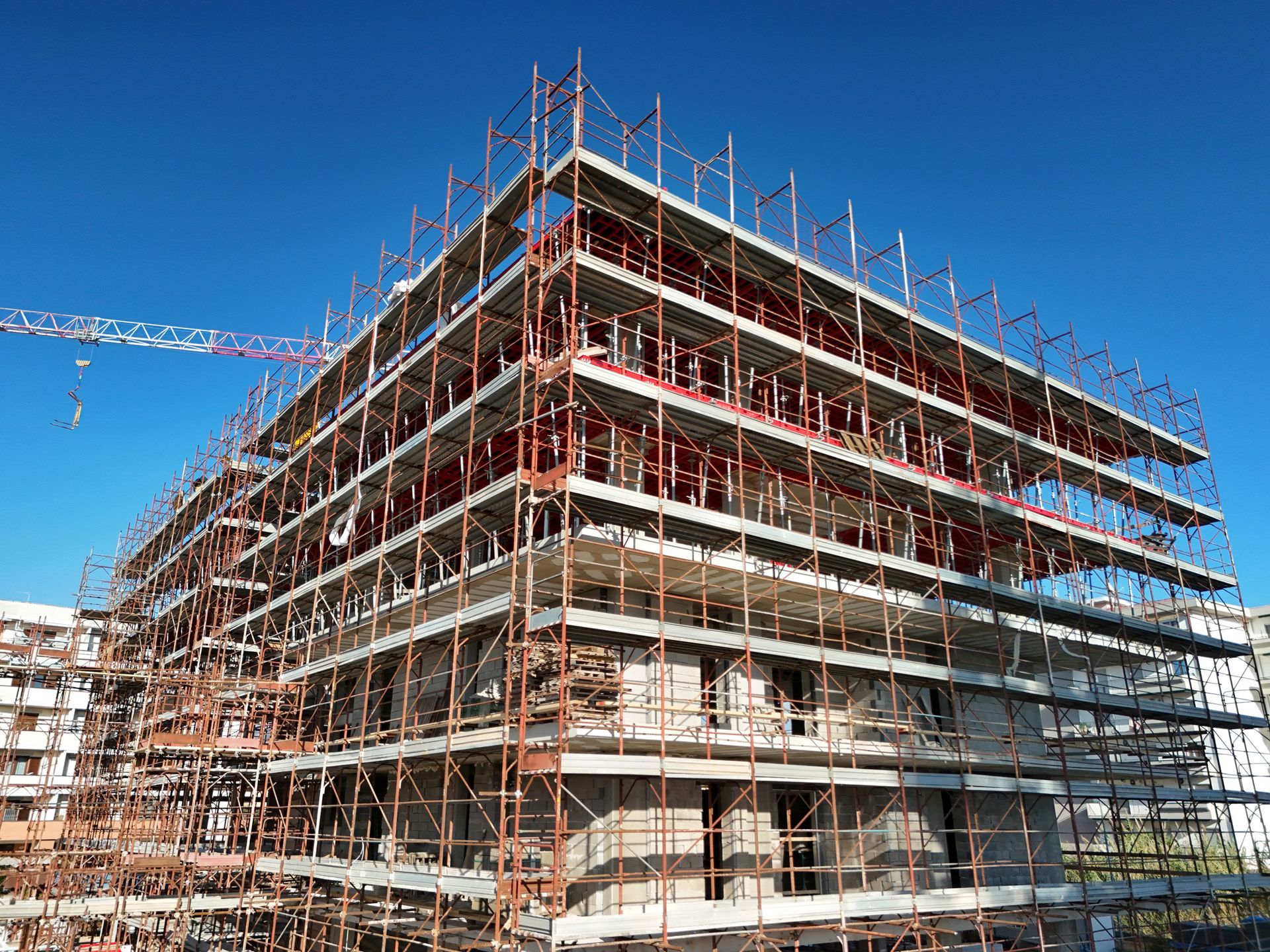 Multi-story building under construction wrapped in scaffolding with a crane against a blue sky