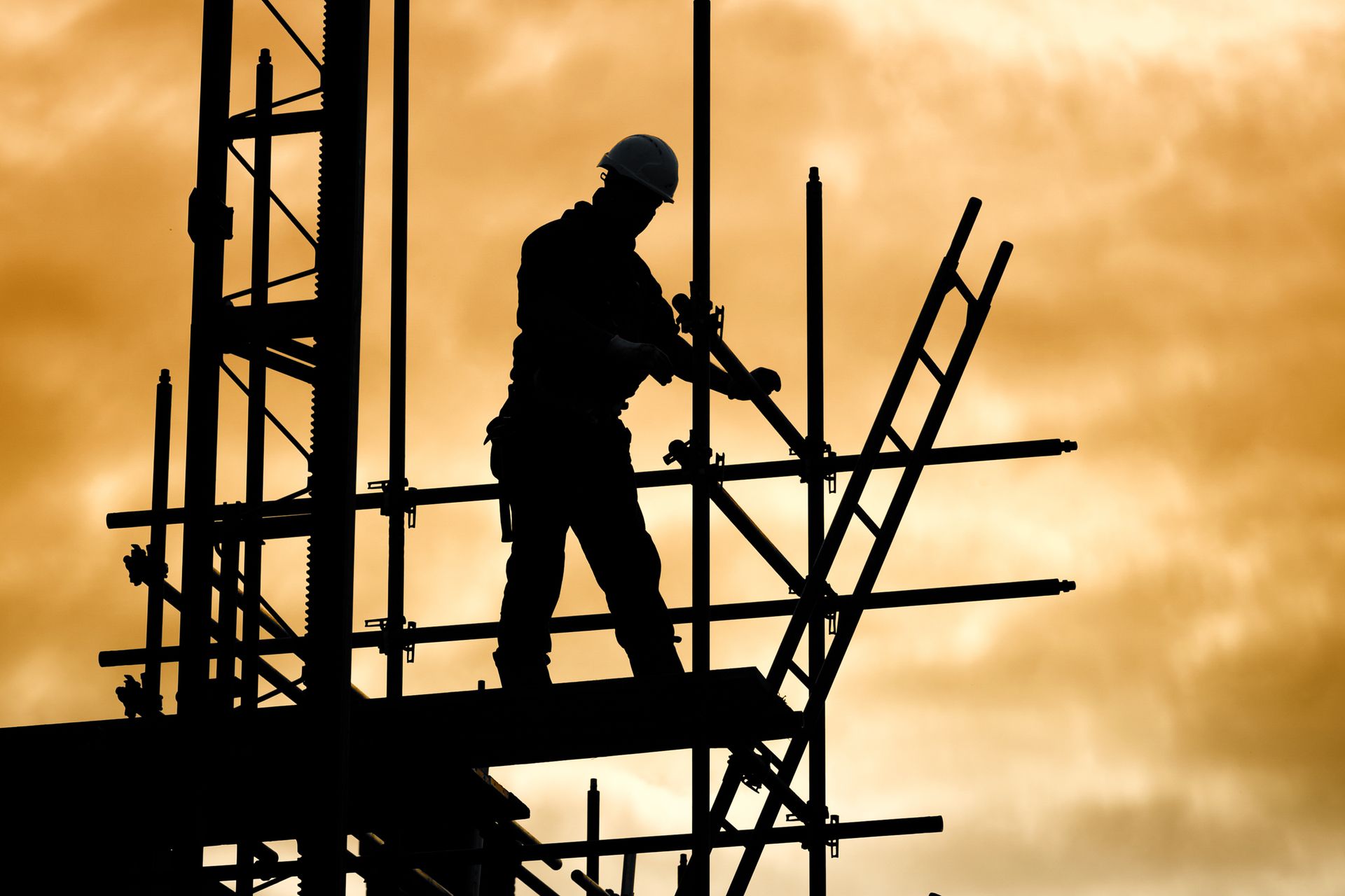 Multi-story building under construction wrapped in scaffolding with a crane against a blue sky