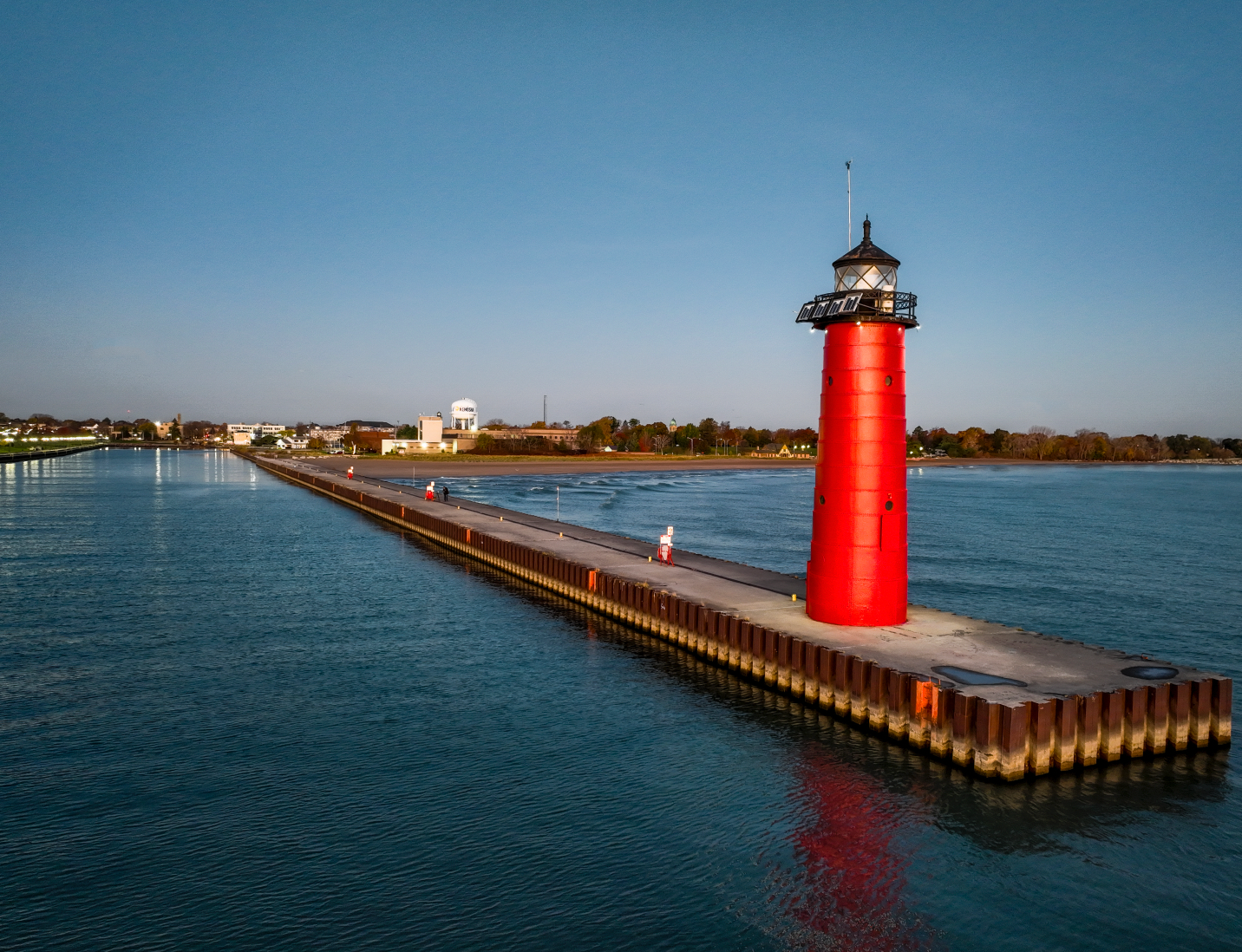 Red lighthouse on a long pier extending into calm blue water at sunset