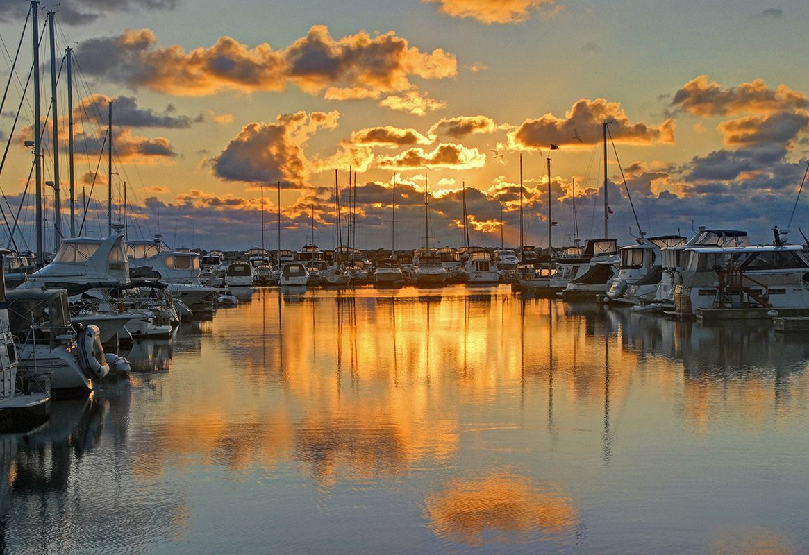 Sunset over a marina with sailboats and golden reflections on calm water