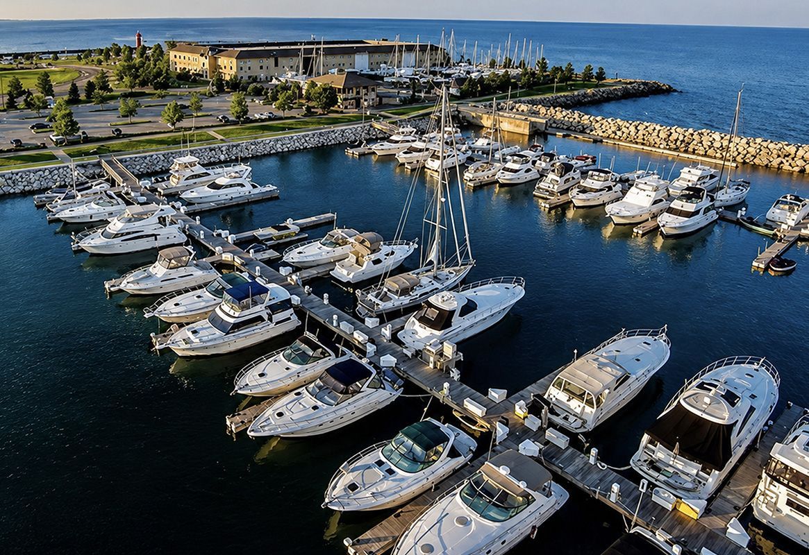 Aerial view of a marina with many docked boats beside a rocky breakwater and blue water.