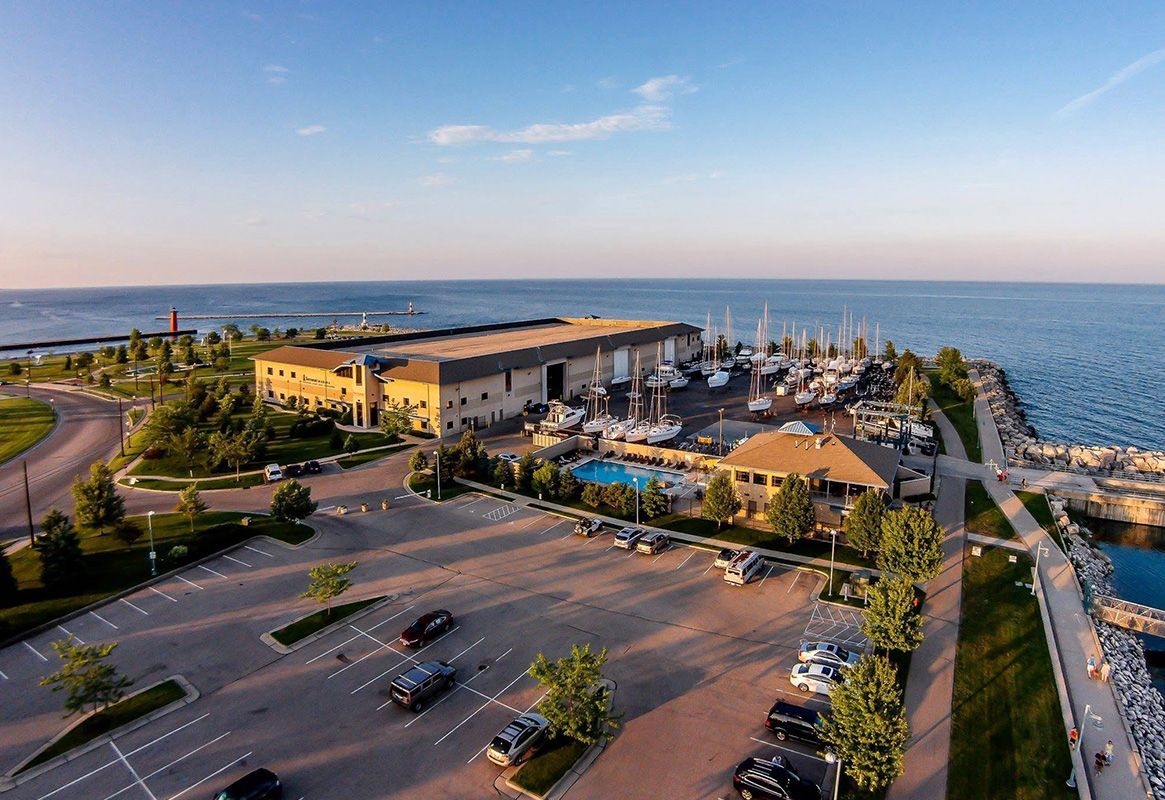 Aerial view of a waterfront resort with parking lot, marina boats, and ocean at sunset