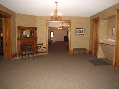 Interior of a room with brown carpet, fireplace, and two doorways. A chandelier hangs from the ceiling.