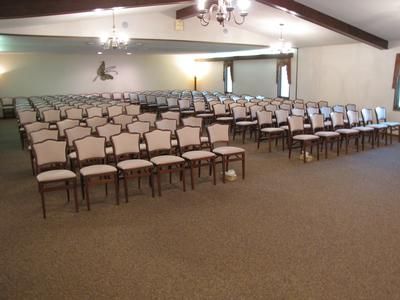 Rows of empty chairs arranged for an event in a large room with a tan carpet.