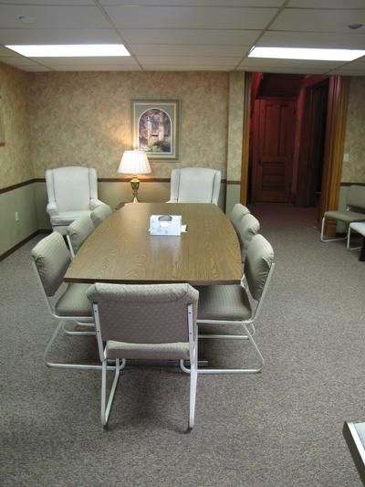 Conference room with a long table, eight chairs, two armchairs, a lamp, and beige carpet.
