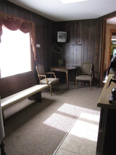 Small waiting room with wood paneling, a bench, two chairs, and a small table.