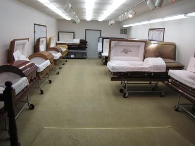 Funeral home showroom with various open and closed caskets on display.