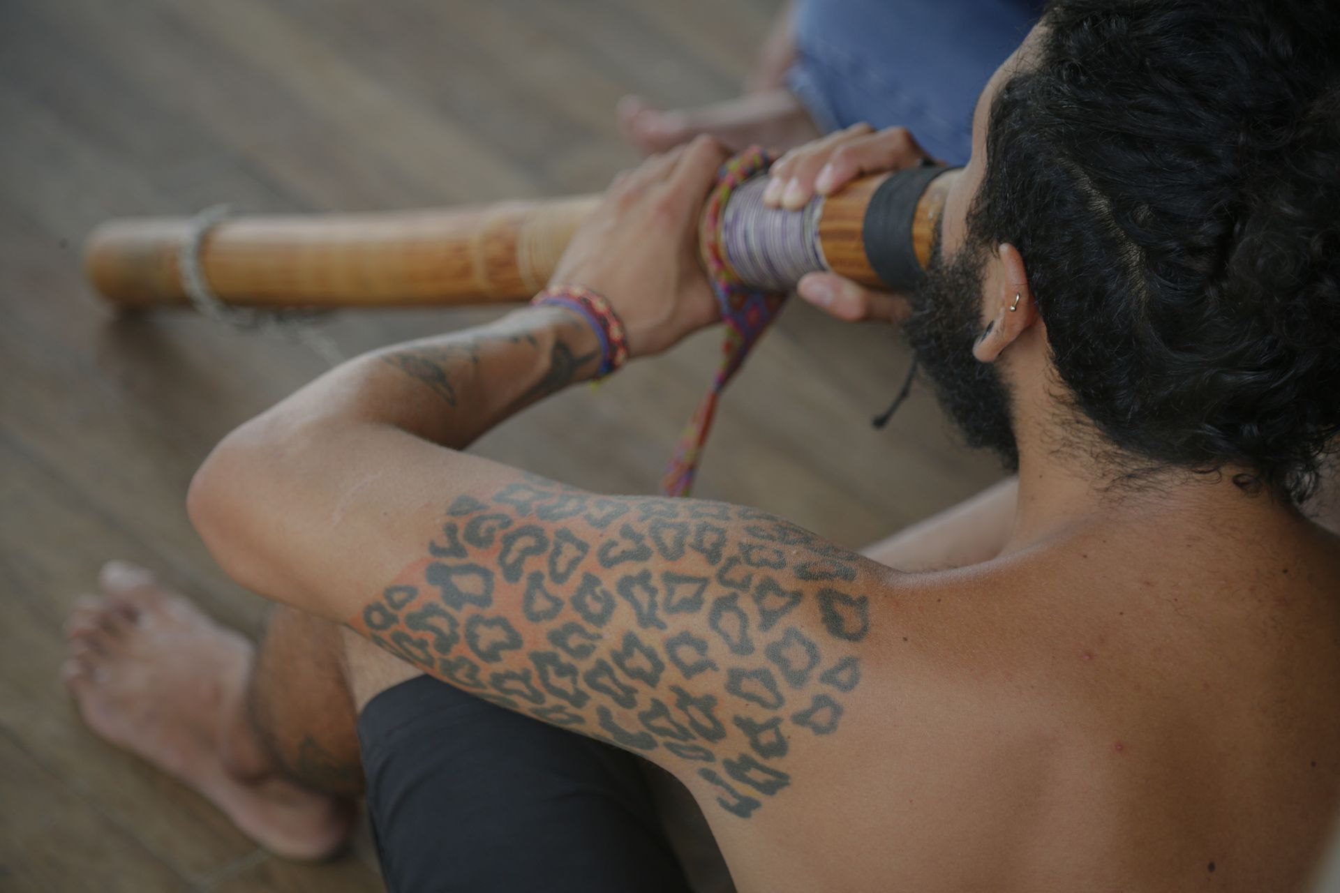 Persona tocando un didgeridoo, tatuaje en el brazo visible.