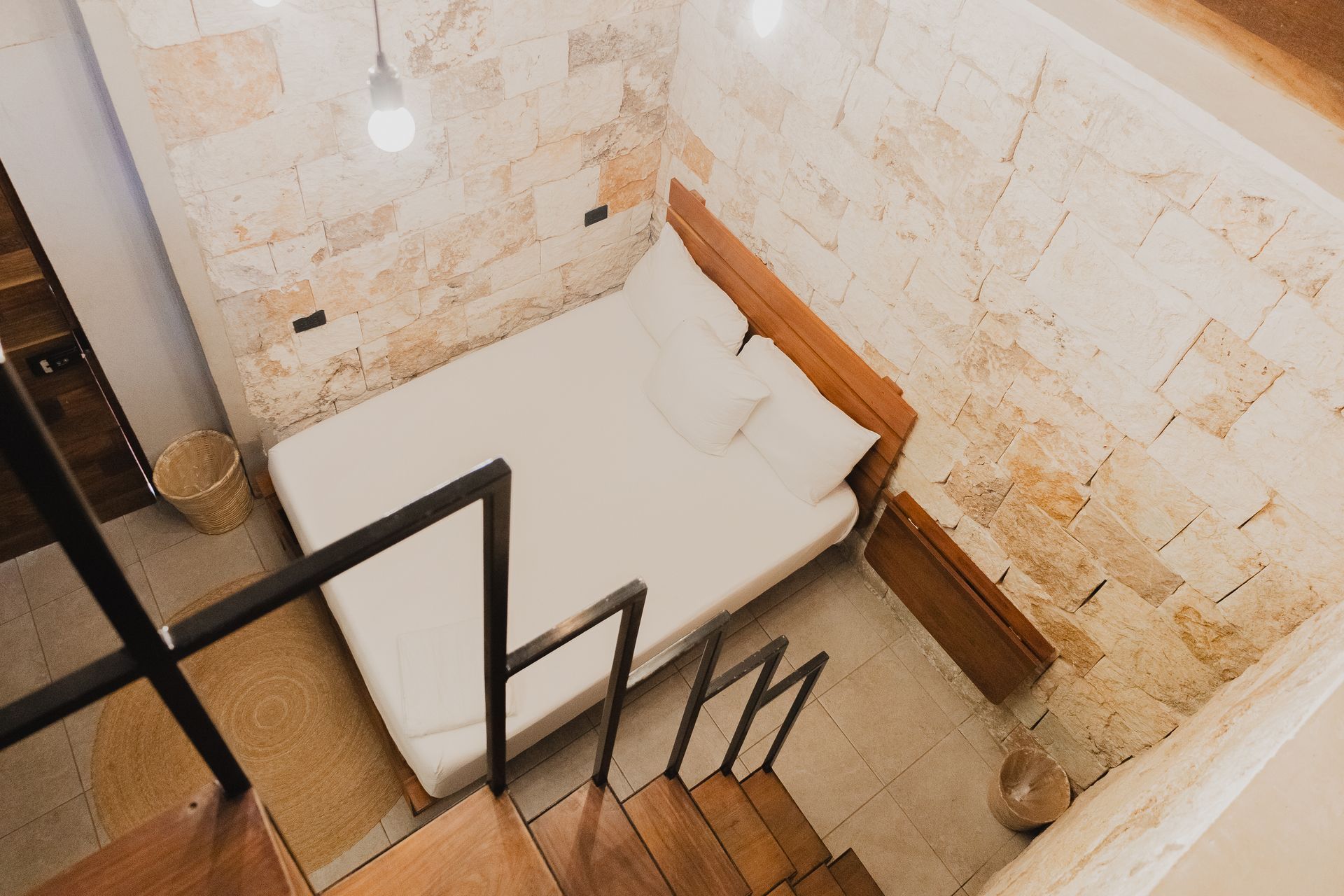 Dormitorio con cama, paredes de ladrillo y escaleras. Vista aérea del interior.