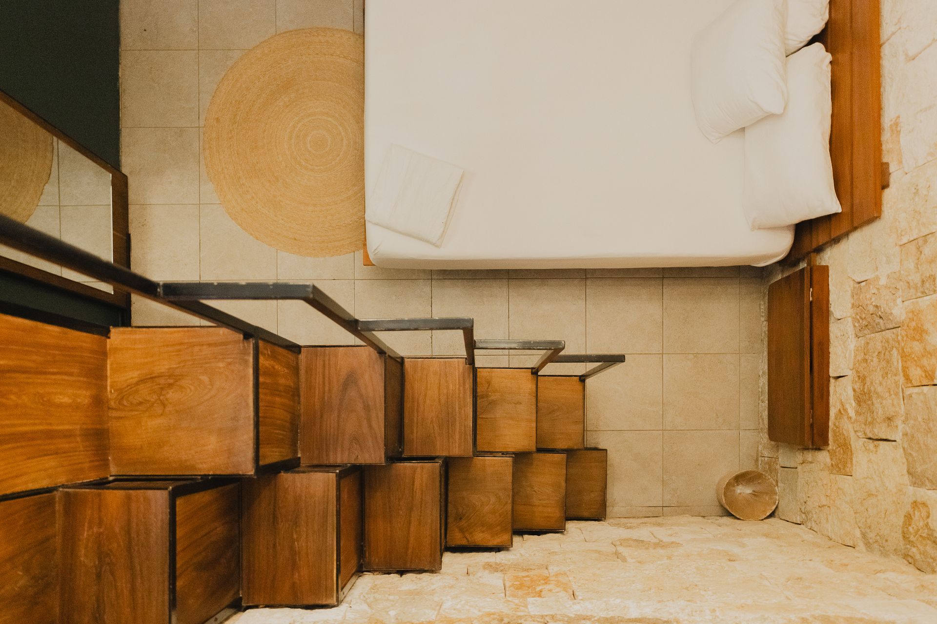 Dormitorio con escalones de madera que conducen a una cama, alfombra color canela y pared de piedra.