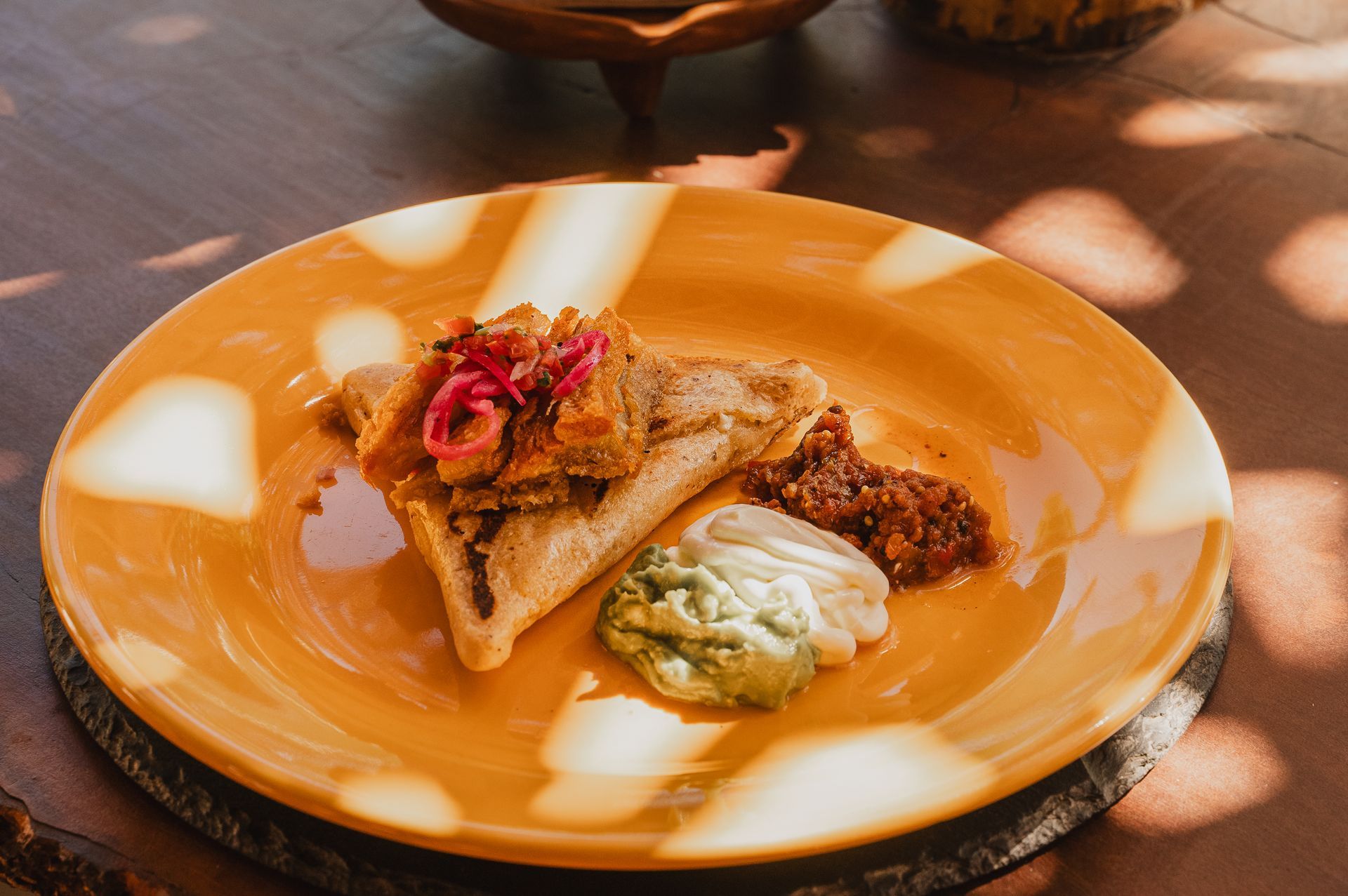 Tamal con aderezos y salsas en un plato naranja, sobre una mesa de madera.