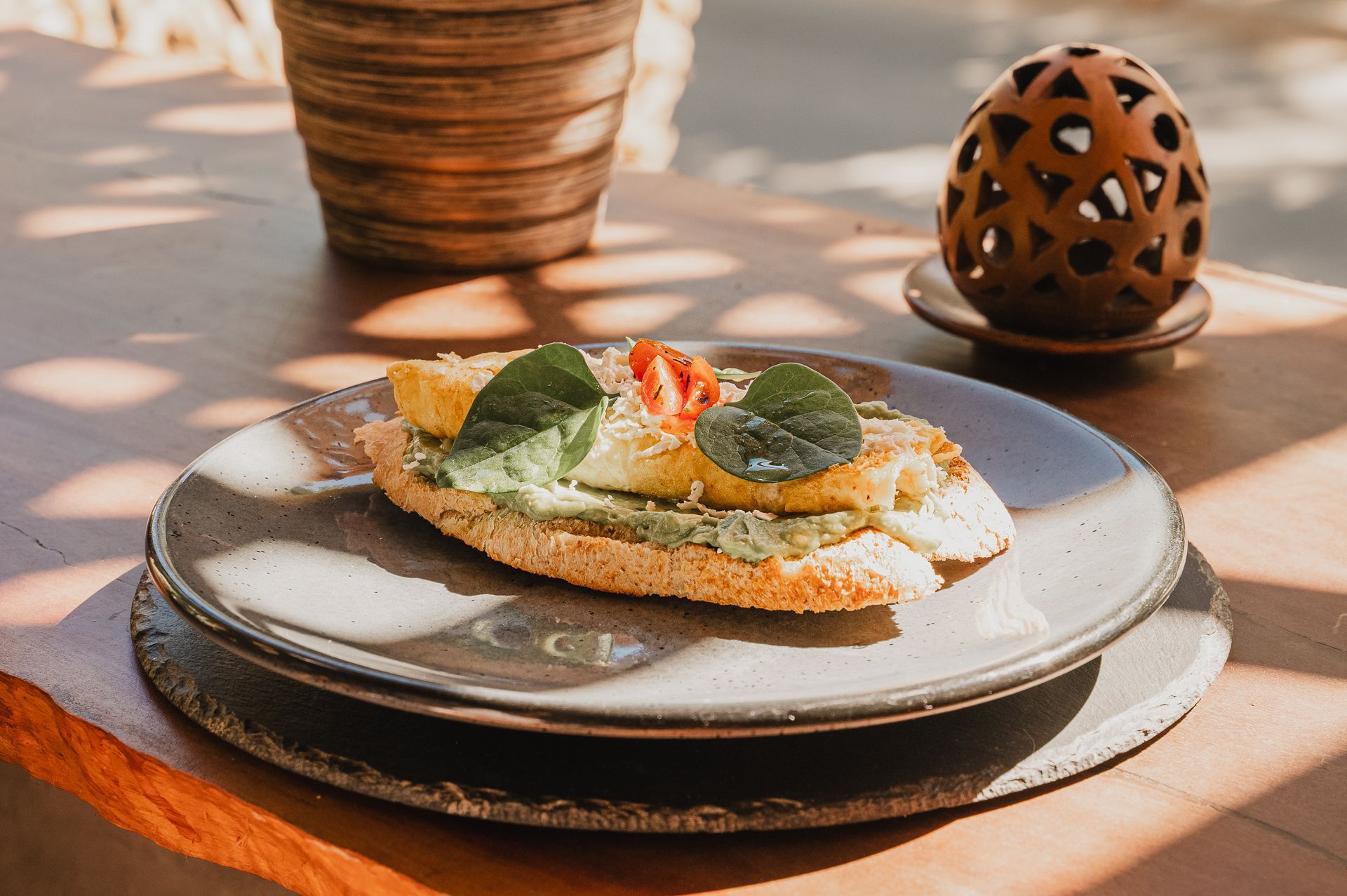 Tostada cubierta con aguacate, huevo frito, tomate y albahaca en un plato.