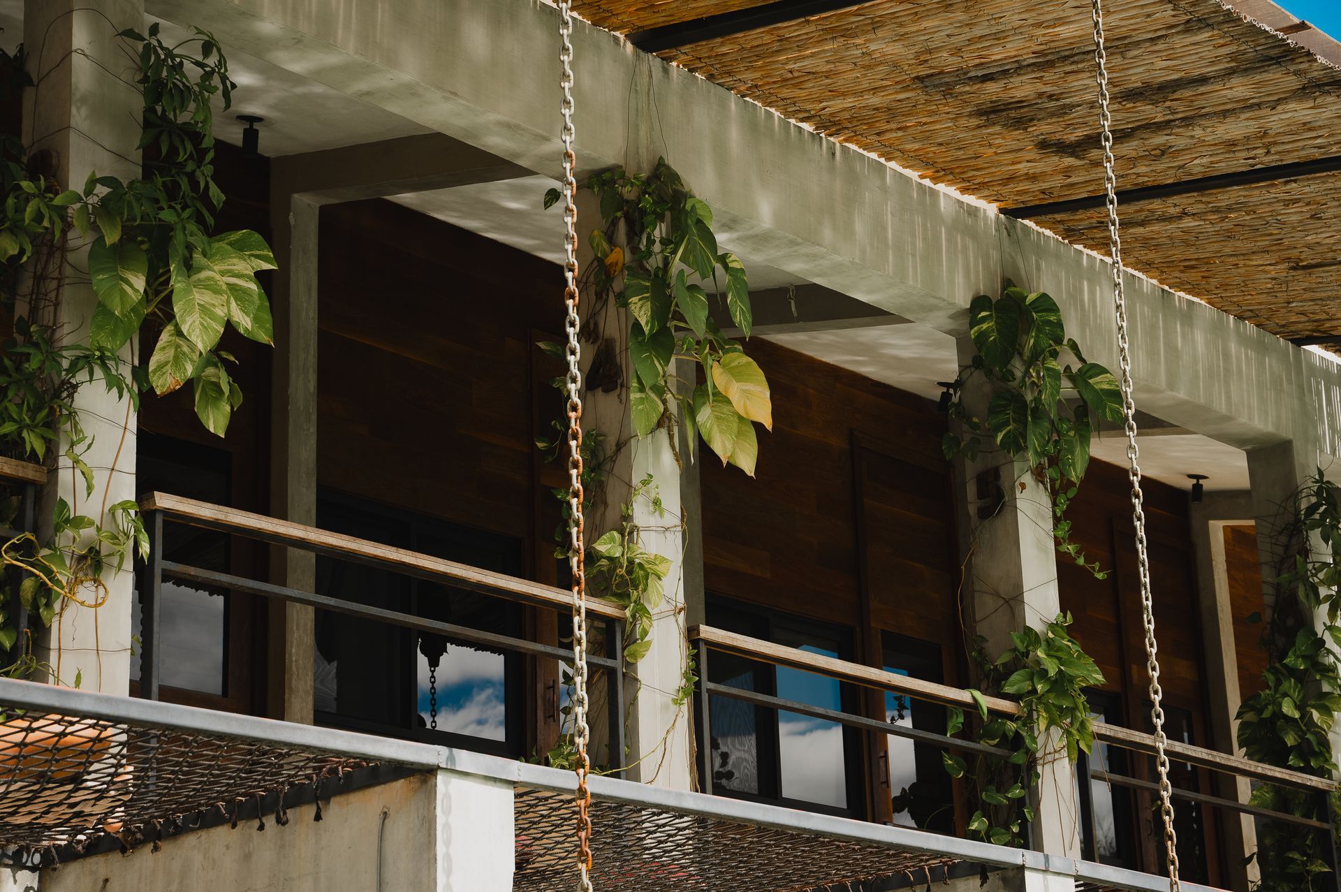 Exterior del edificio con plantas, contraventanas de madera y techo tejido.