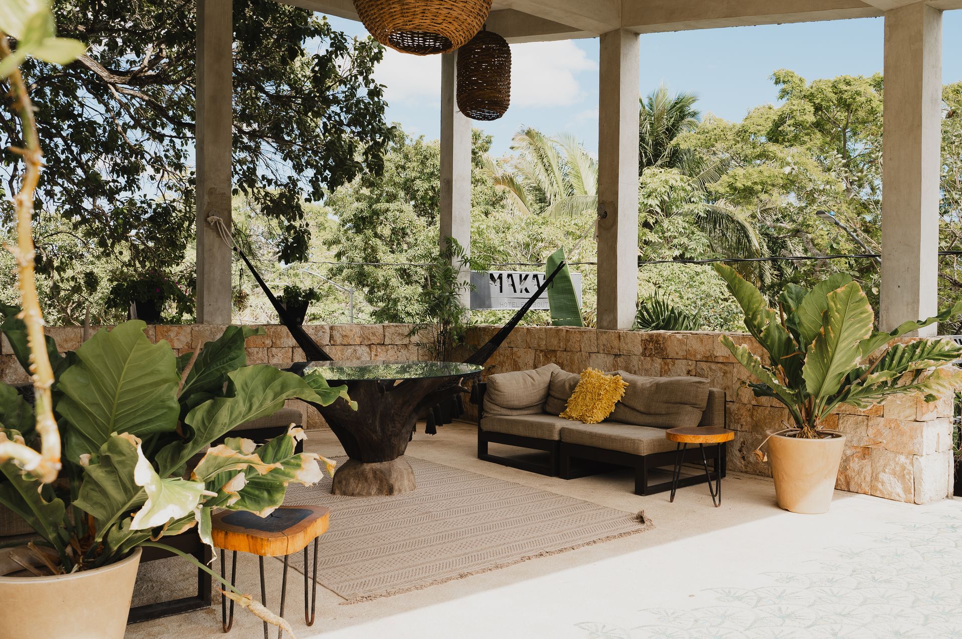 Patio cubierto con plantas, sofá, alfombra y hamaca, con vista a una exuberante vegetación.