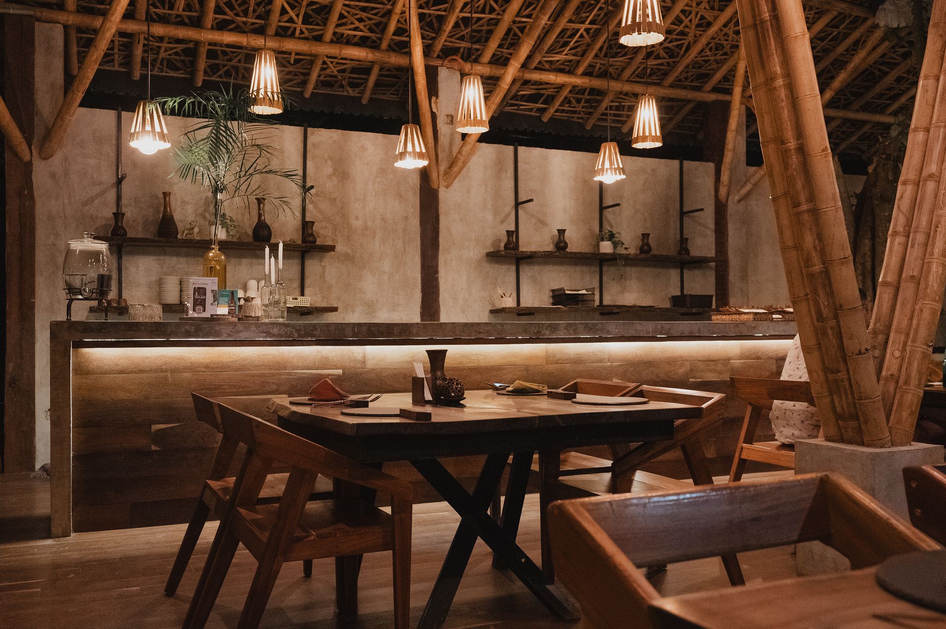 Vista interior de un restaurante construido con bambú con mesas de madera, sillas y lámparas colgantes.
