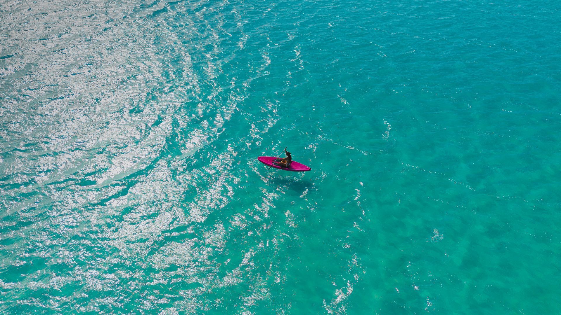 Persona en una tabla de paddle surf rosa en aguas turquesas claras.
