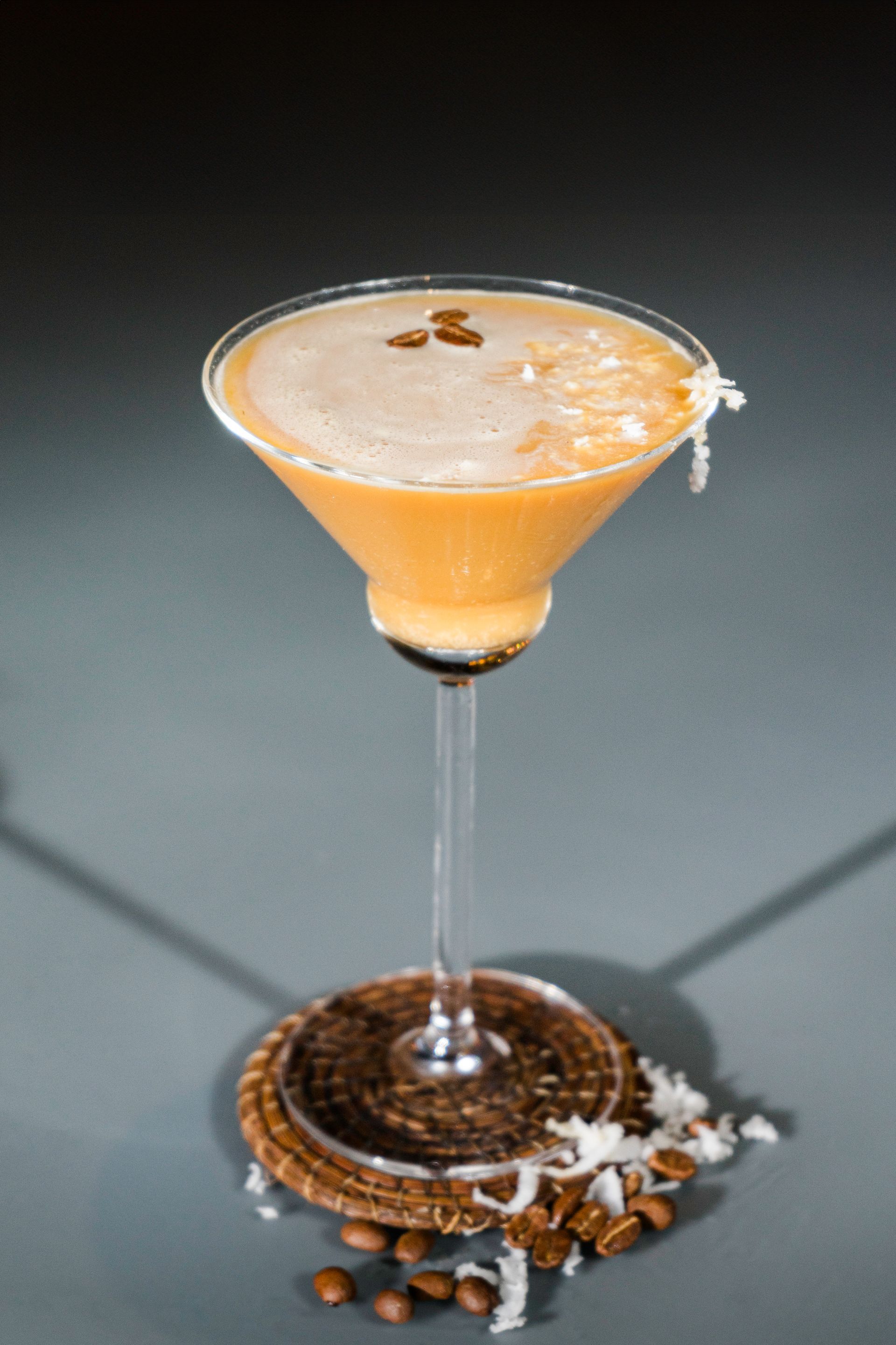 Cóctel de café en copa de martini, adornado con granos de café y hojuelas de coco.