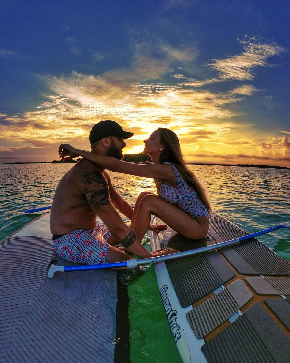Pareja abrazándose en una tabla de remo al atardecer, uno frente al otro y con los brazos alrededor del otro.