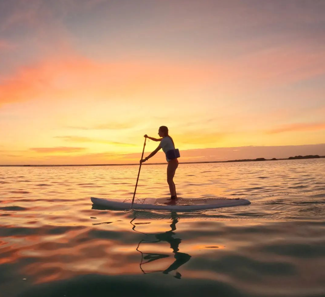 Persona haciendo paddleboarding en aguas tranquilas al atardecer.