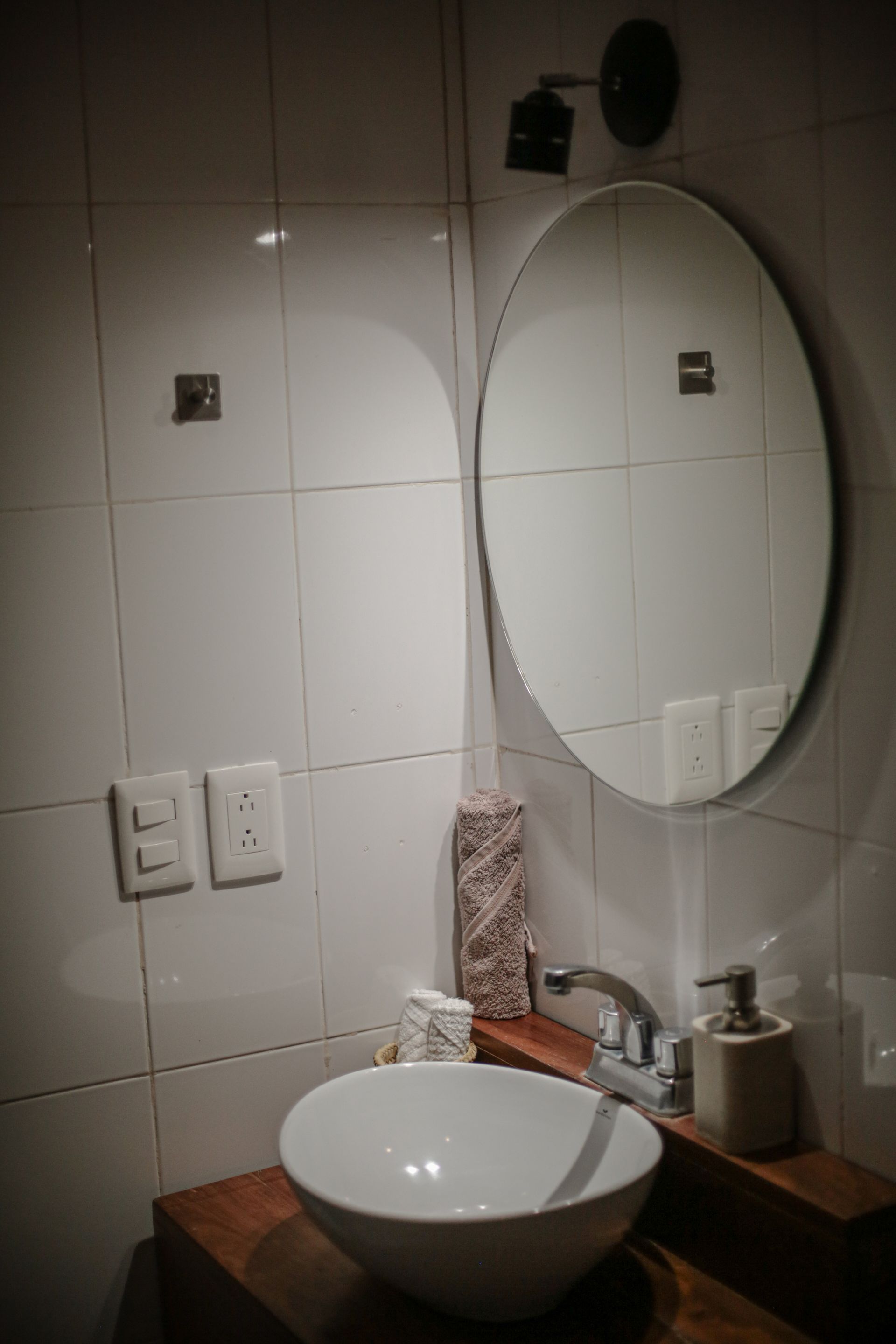 Lavabo de baño blanco bajo espejo ovalado con dispensador de jabón y recipiente decorativo.