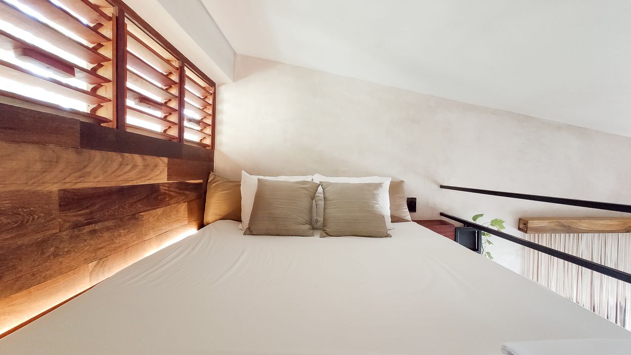 Dormitorio con cama. Pared de madera, ventana con contraventanas y zona de loft.