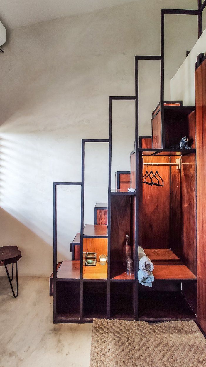 Escalera de madera con espacio de almacenamiento integrado en una habitación. La escalera tiene una estructura metálica negra.