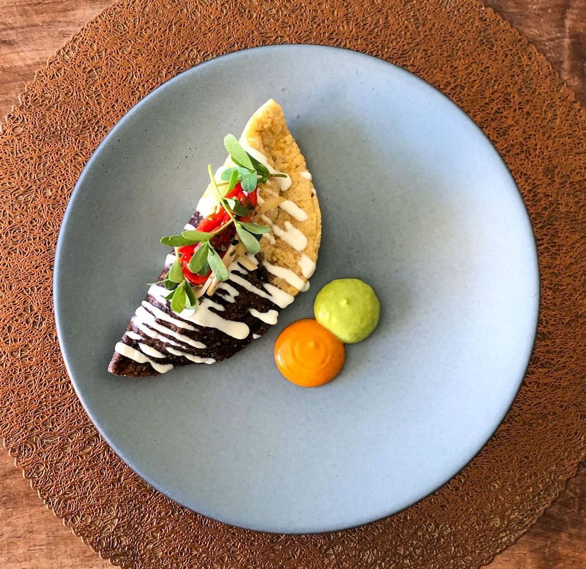 Un taco gourmet con puntos de salsa, plato azul claro sobre un mantel marrón.