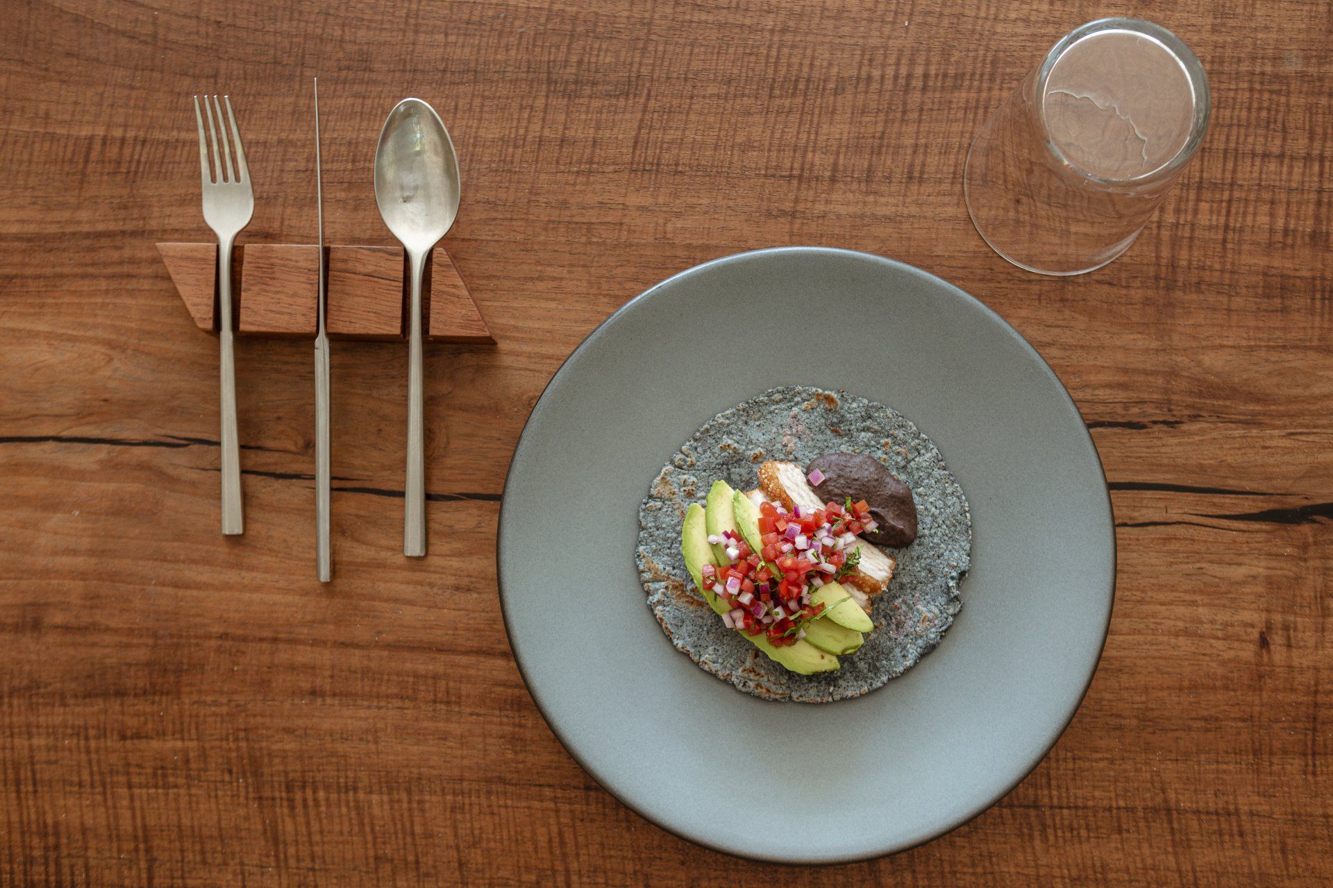 Taco en un plato azul, con cubiertos y una bebida en una mesa de madera.
