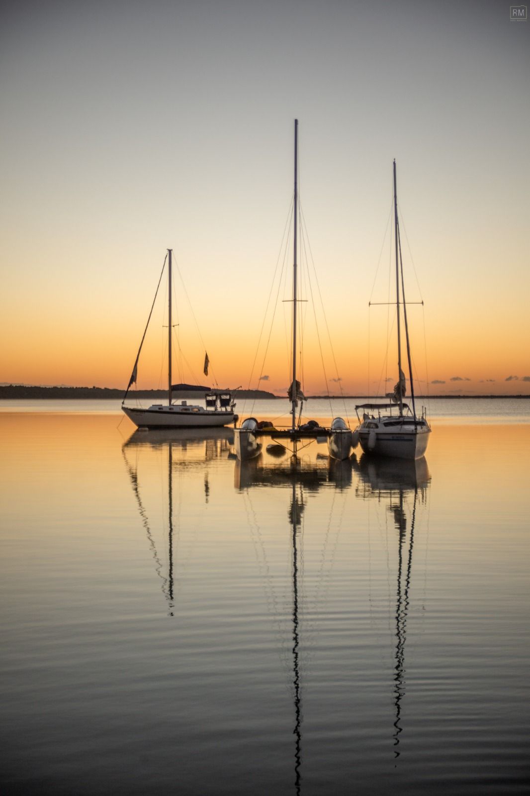 Tres veleros reflejados en aguas tranquilas al atardecer.
