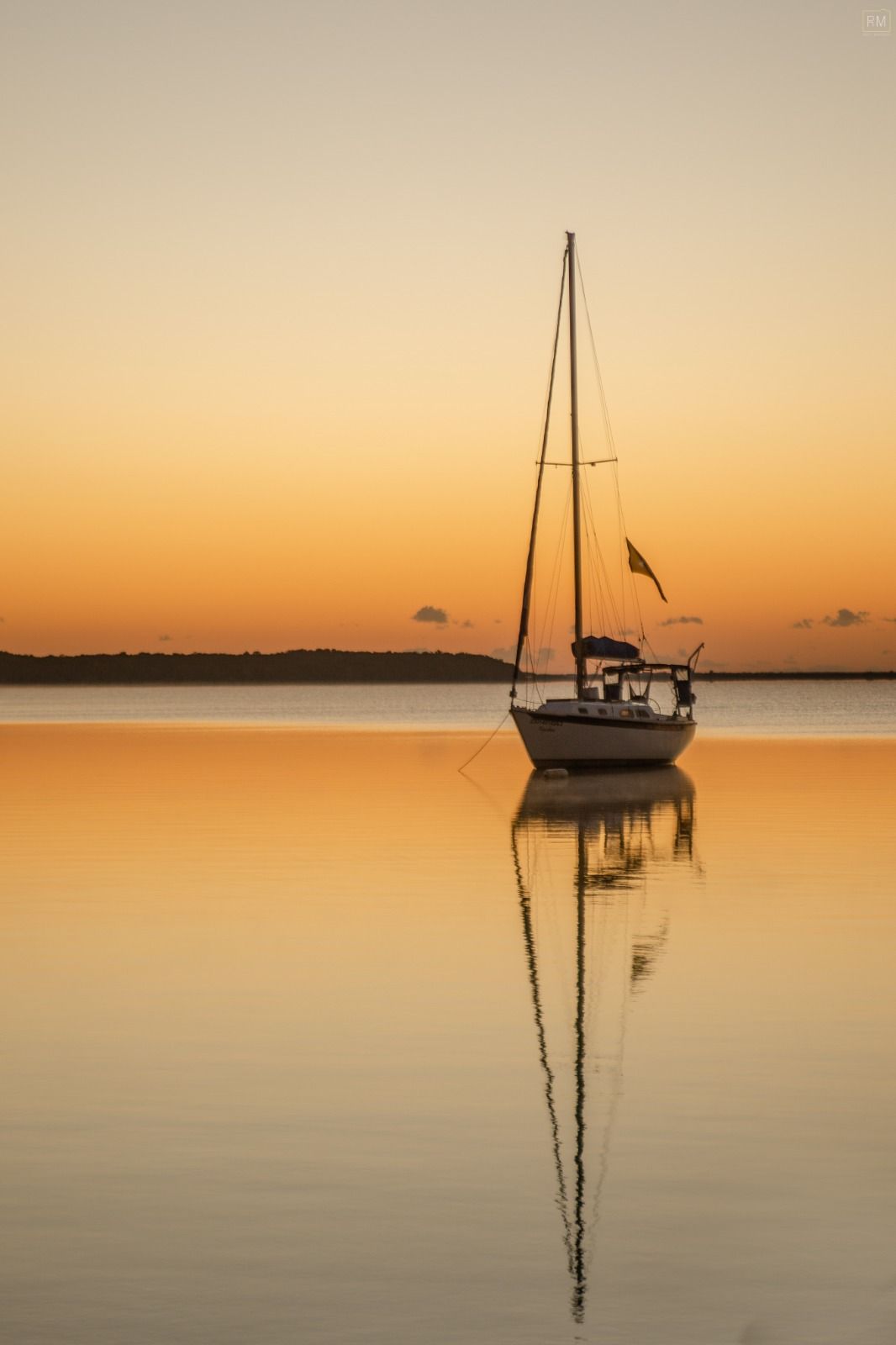 Velero en aguas tranquilas reflejando una puesta de sol dorada.
