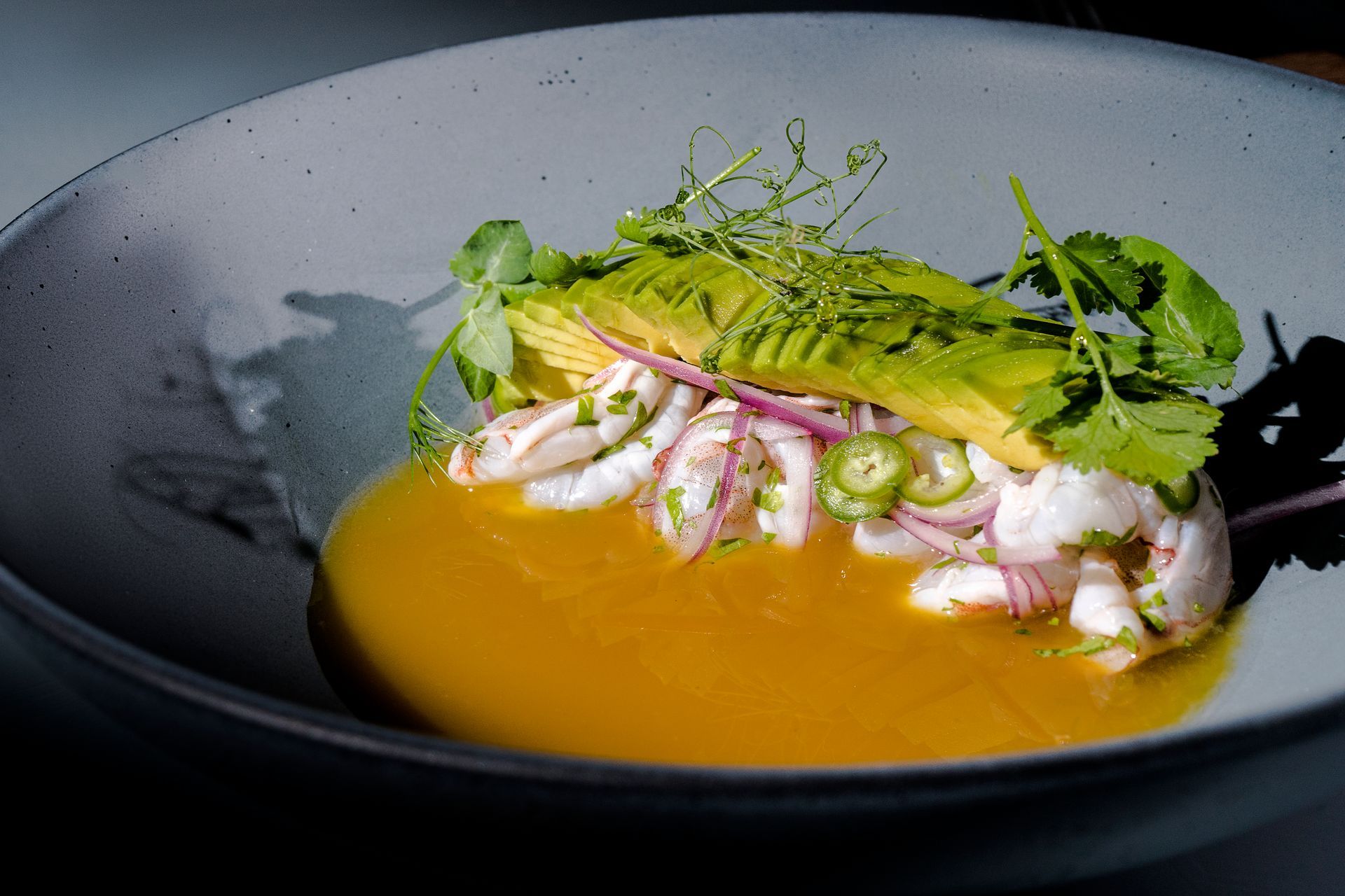 Ceviche en un tazón gris, con aguacate, cilantro, cebolla morada y jalapeños. Caldo de color naranja brillante.