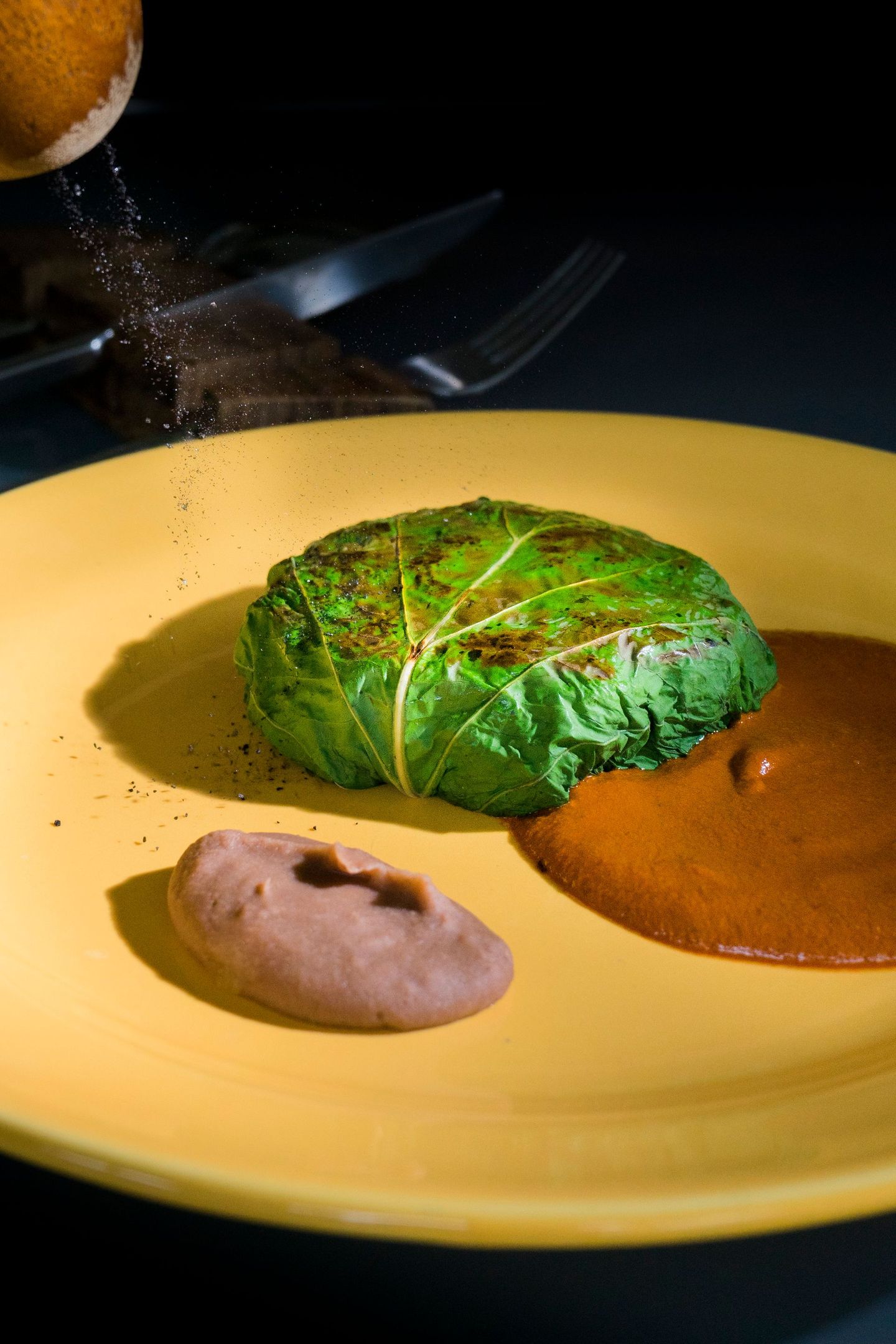 Comida envuelta en verde en un plato amarillo con salsa marrón y condimentos espolvoreados.
