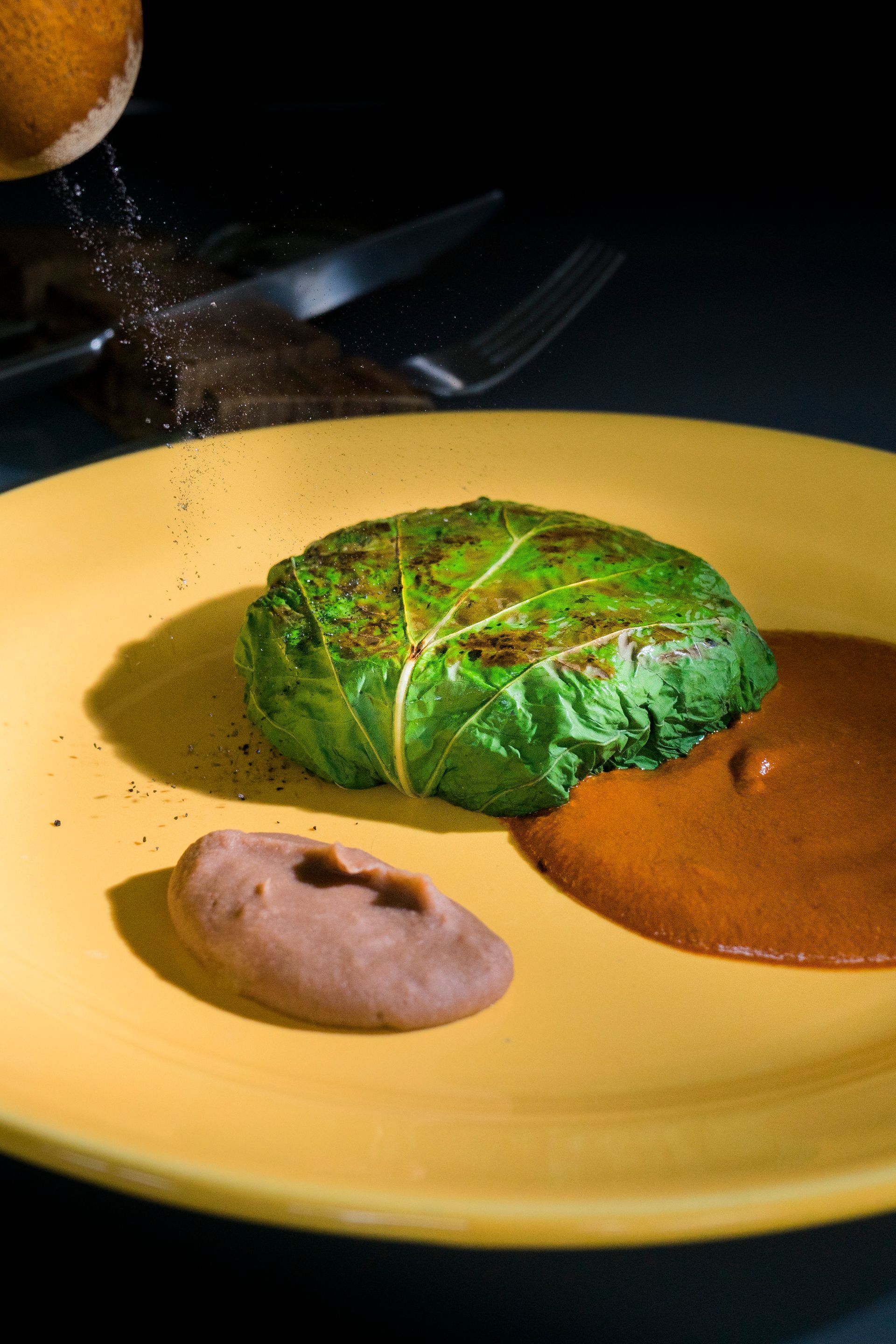 Comida envuelta en verde en un plato amarillo con salsa marrón y condimentos espolvoreados.