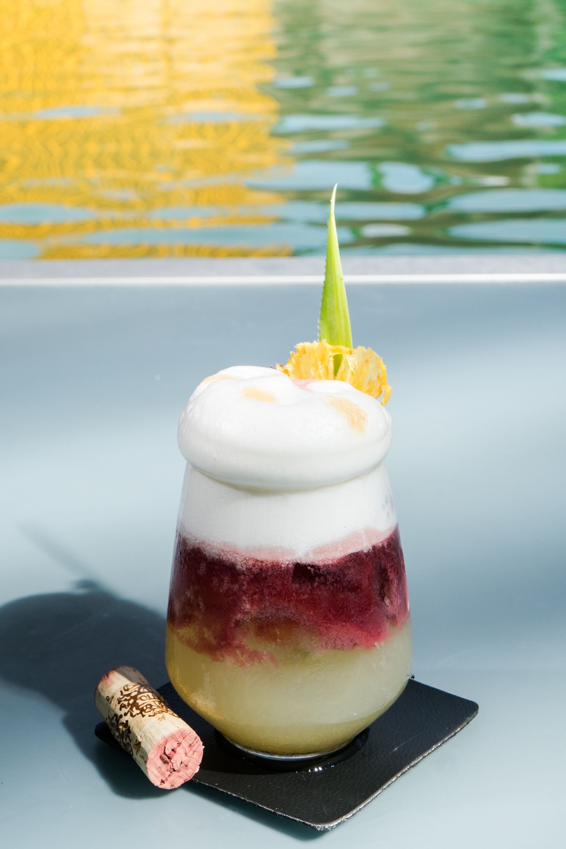 Cóctel en capas en copa, con espuma y decoración de piña.