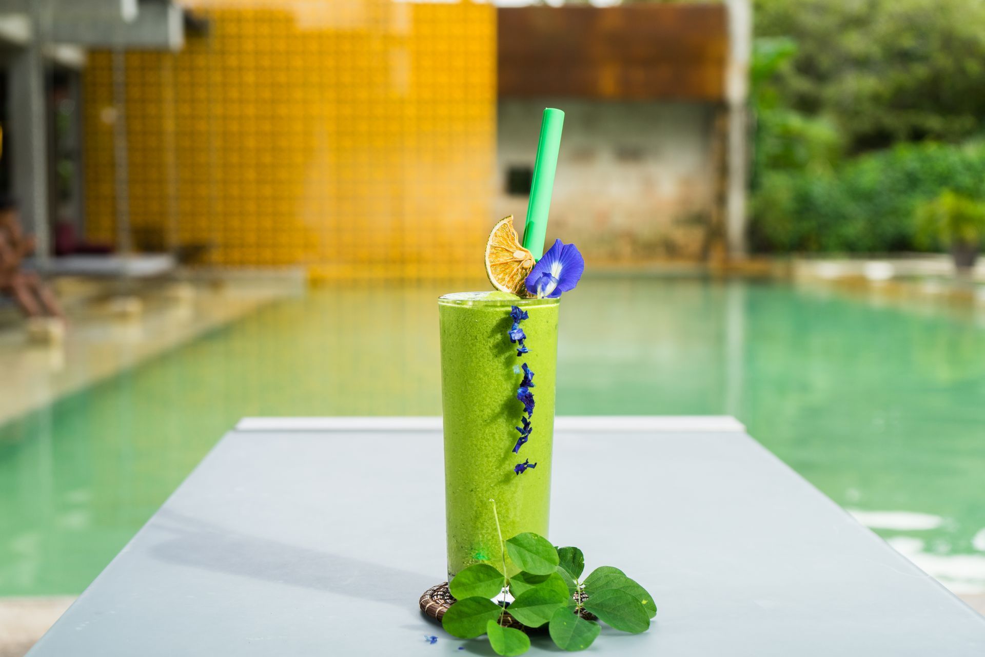 Batido verde con guarnición en la mesa, piscina de fondo.