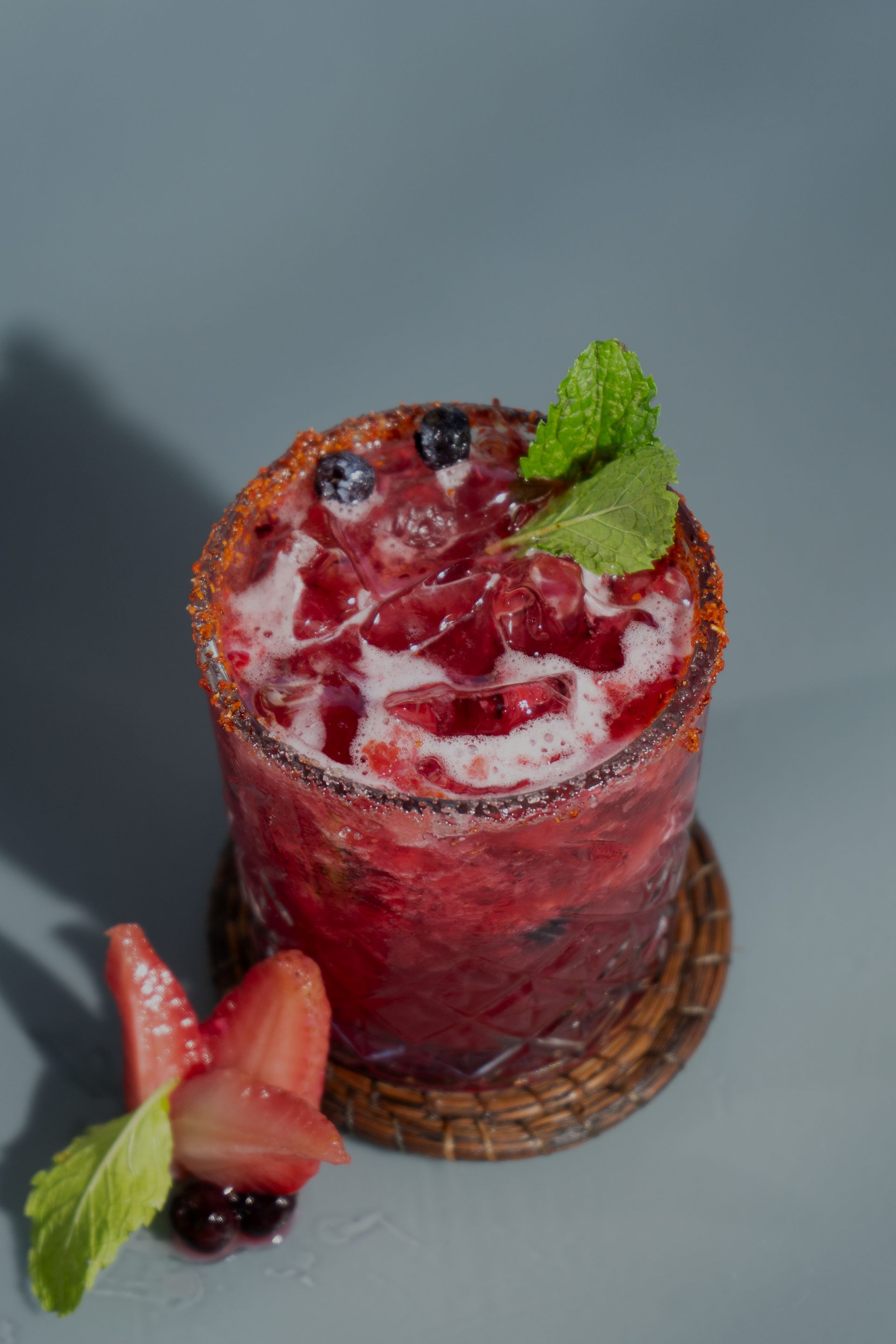 Cóctel de bayas adornado con menta, arándanos y fresas, sobre un posavasos tejido.