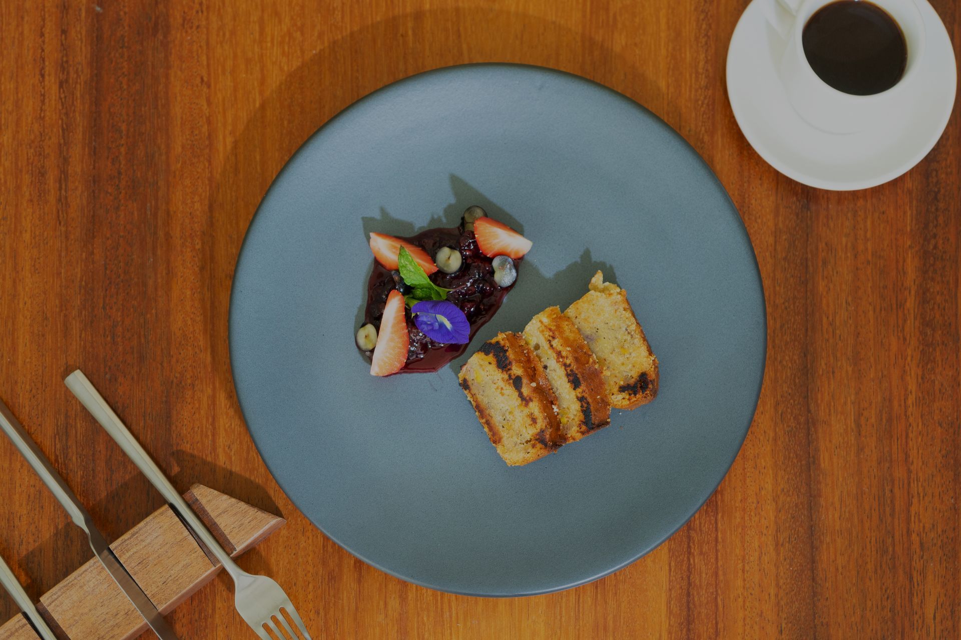 Tostada francesa con compota de bayas, fresas y café sobre una mesa de madera.