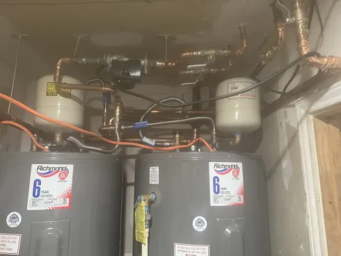 Basement utility area with two water heaters, pipes, valves, and an expansion tank above.