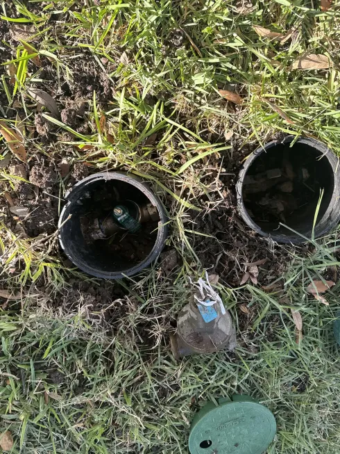 Two black pipes in grass with a small green lid nearby