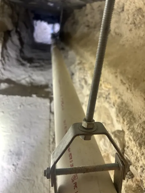 Close-up of a cable anchor and threaded rod inside a narrow stone-lined shaft.