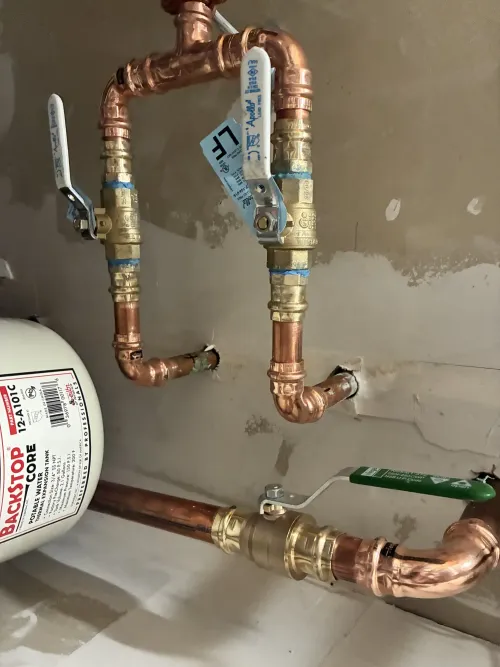 Copper plumbing pipes with blue valve handles and a white water heater in a utility area