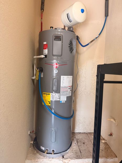 Two gray water heaters in a utility closet with copper pipes and an expansion tank.
