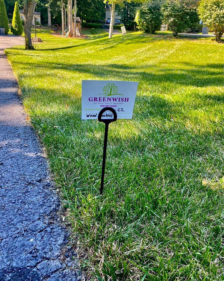 A Greenwish lawn sign planted in a green grass yard next to an asphalt driveway.