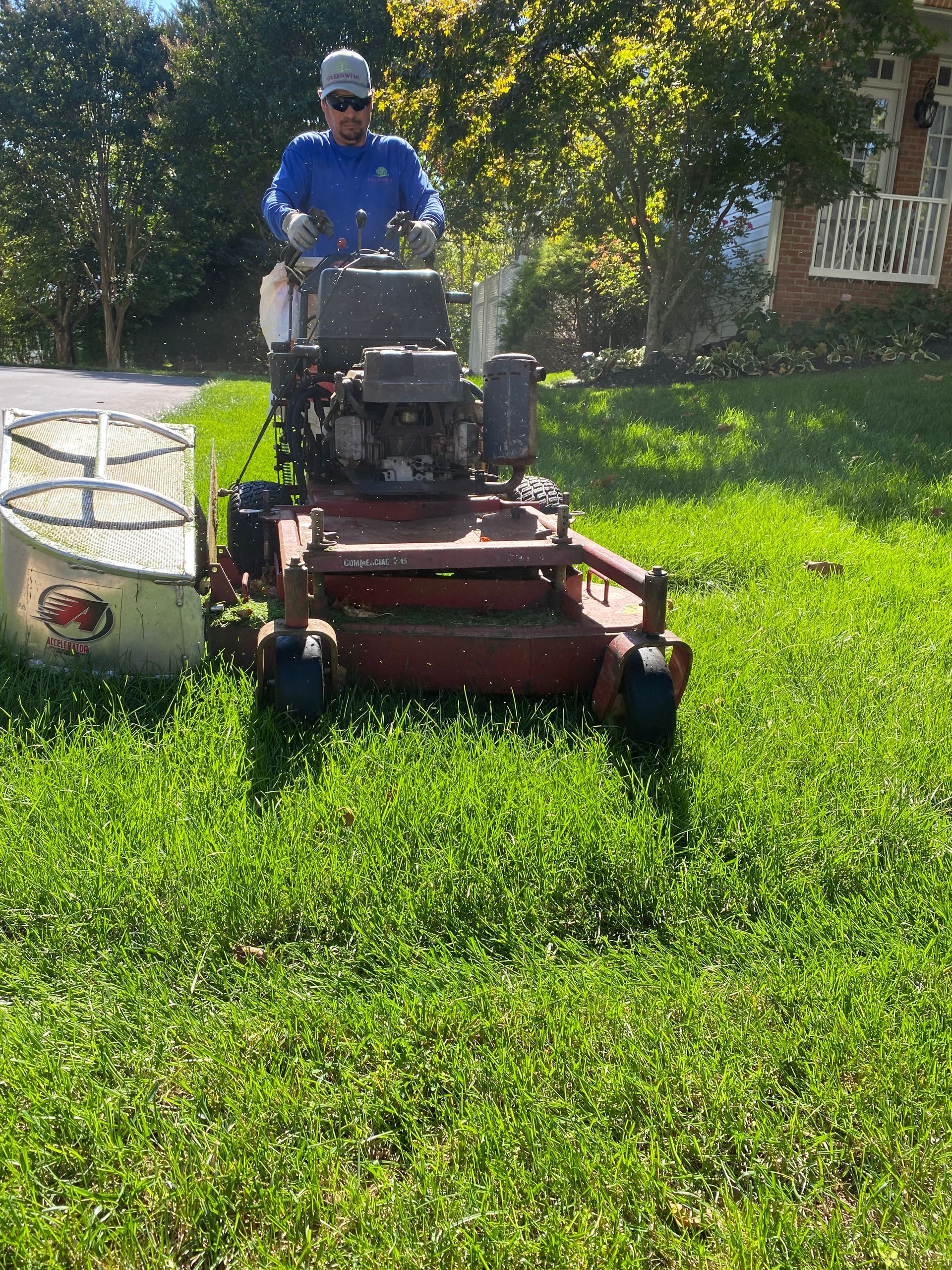 A person wearing a blue shirt and hat operates a red commercial lawn mower on a grassy residential lawn.