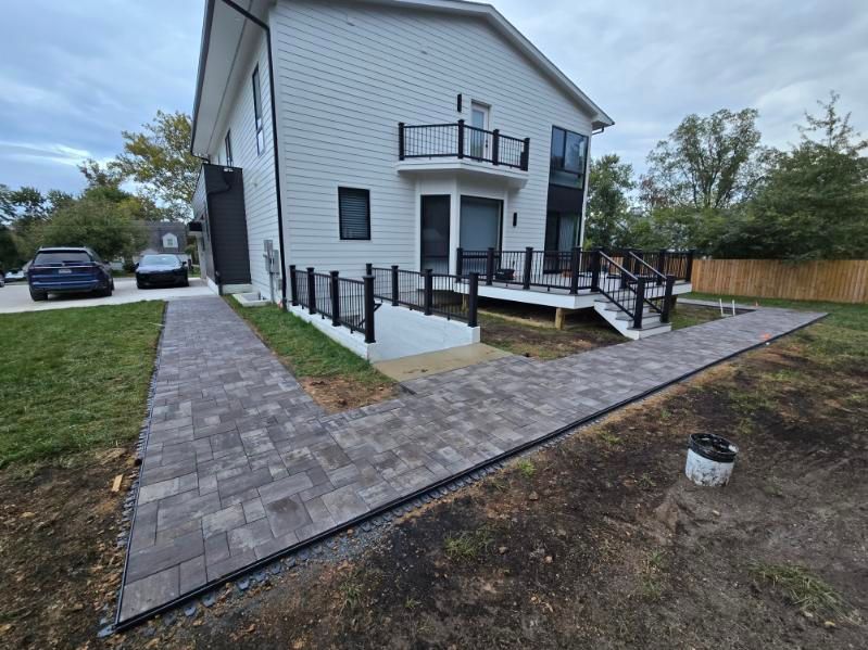 White two-story house with front ramp, black railings, and brick walkway in a yard under construction