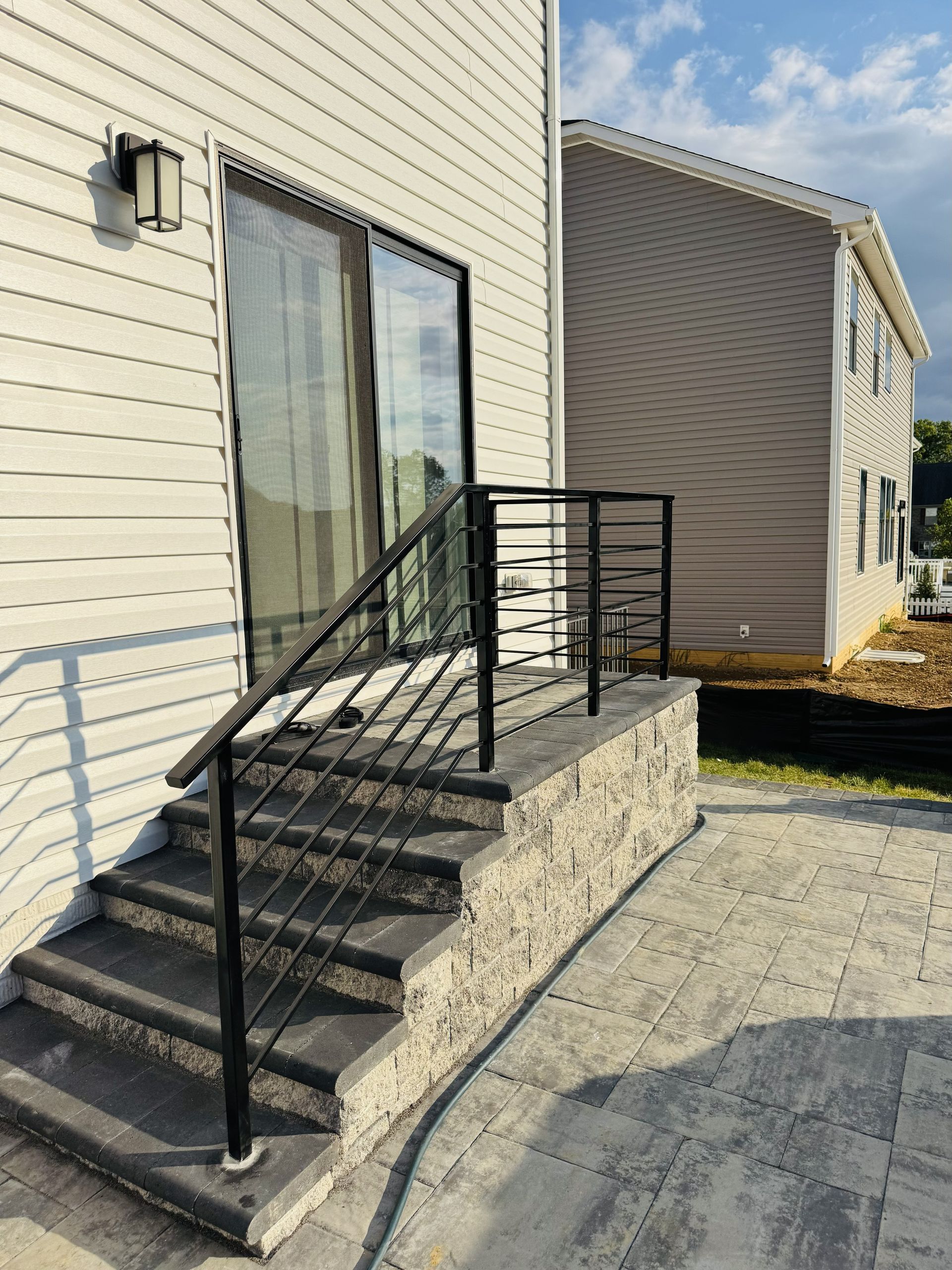 A set of outdoor stone steps with a black metal railing leading up to a sliding glass door on a light-sided house.