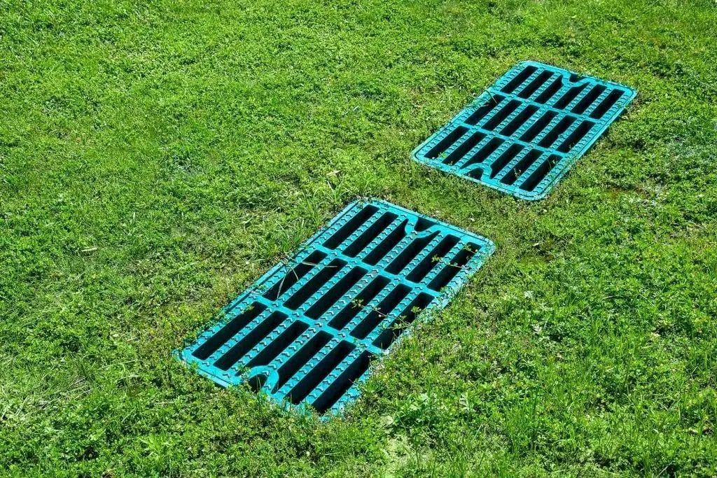 Two rectangular green plastic drainage grates set into a patch of green grass.