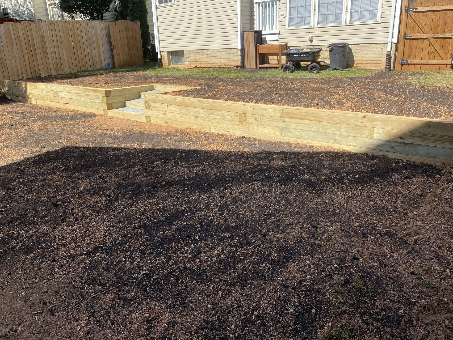 A newly installed wooden retaining wall with steps in a backyard covered in fresh dark mulch.