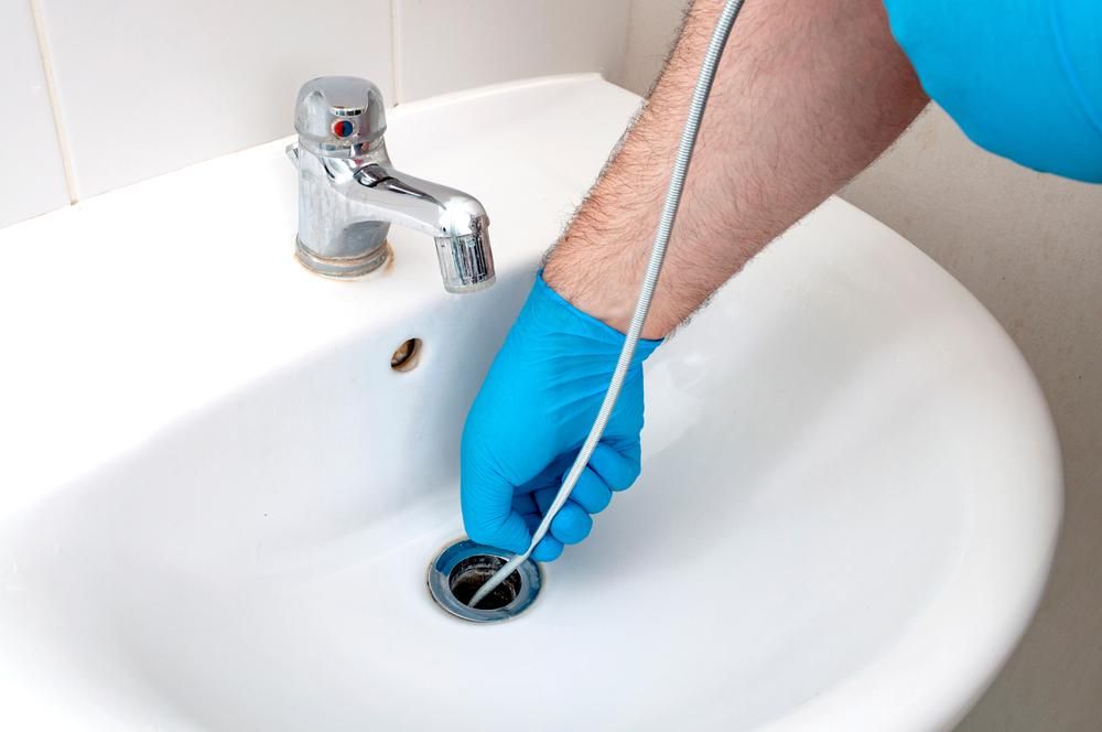 A Man in Blue Gloves is Cleaning a Sink With a Hose — Jet 'N' Drain Pty Ltd In Kawungan, QLD