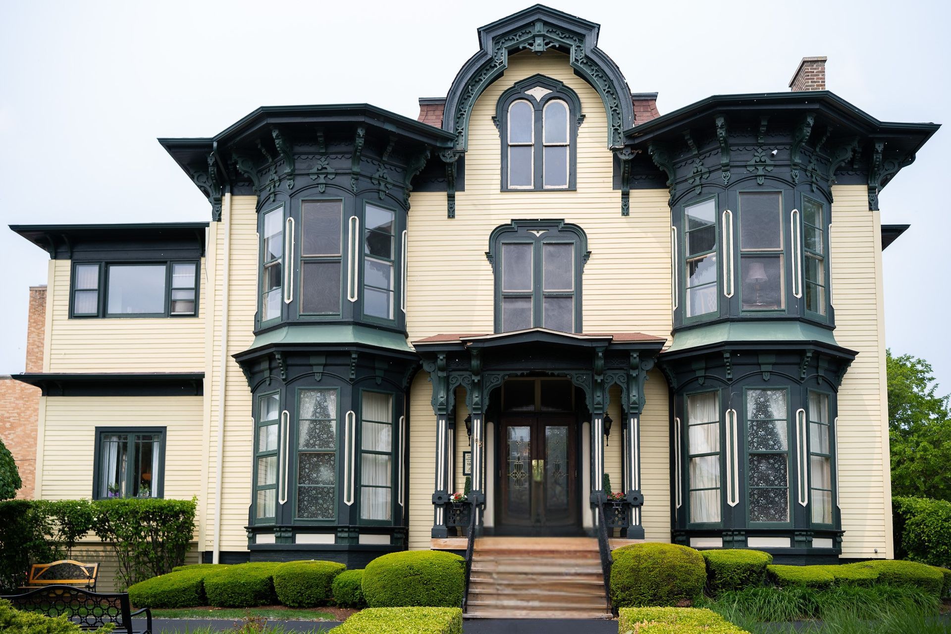 Victorian-style cream house with dark trim, ornate bay windows, and a centered front entrance